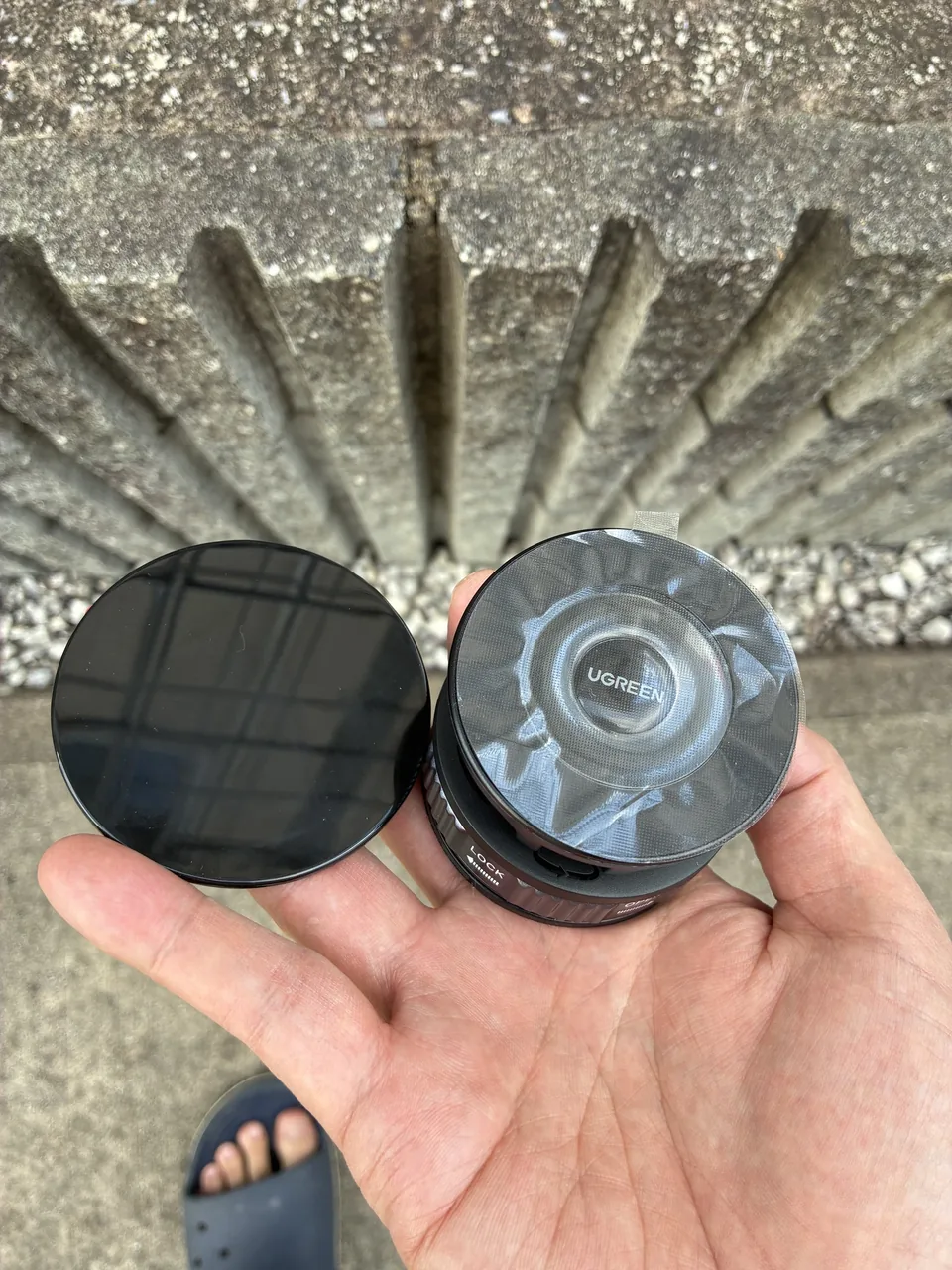 手のひらに載せて広げたUGREENホルダー。黒い丸い面とUGREENの文字がある丸い面が見える。